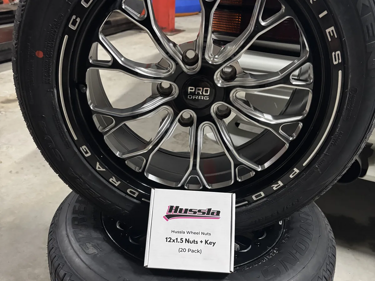 Two black and machined alloy wheels with tyres fitted, stacked in the workshop.