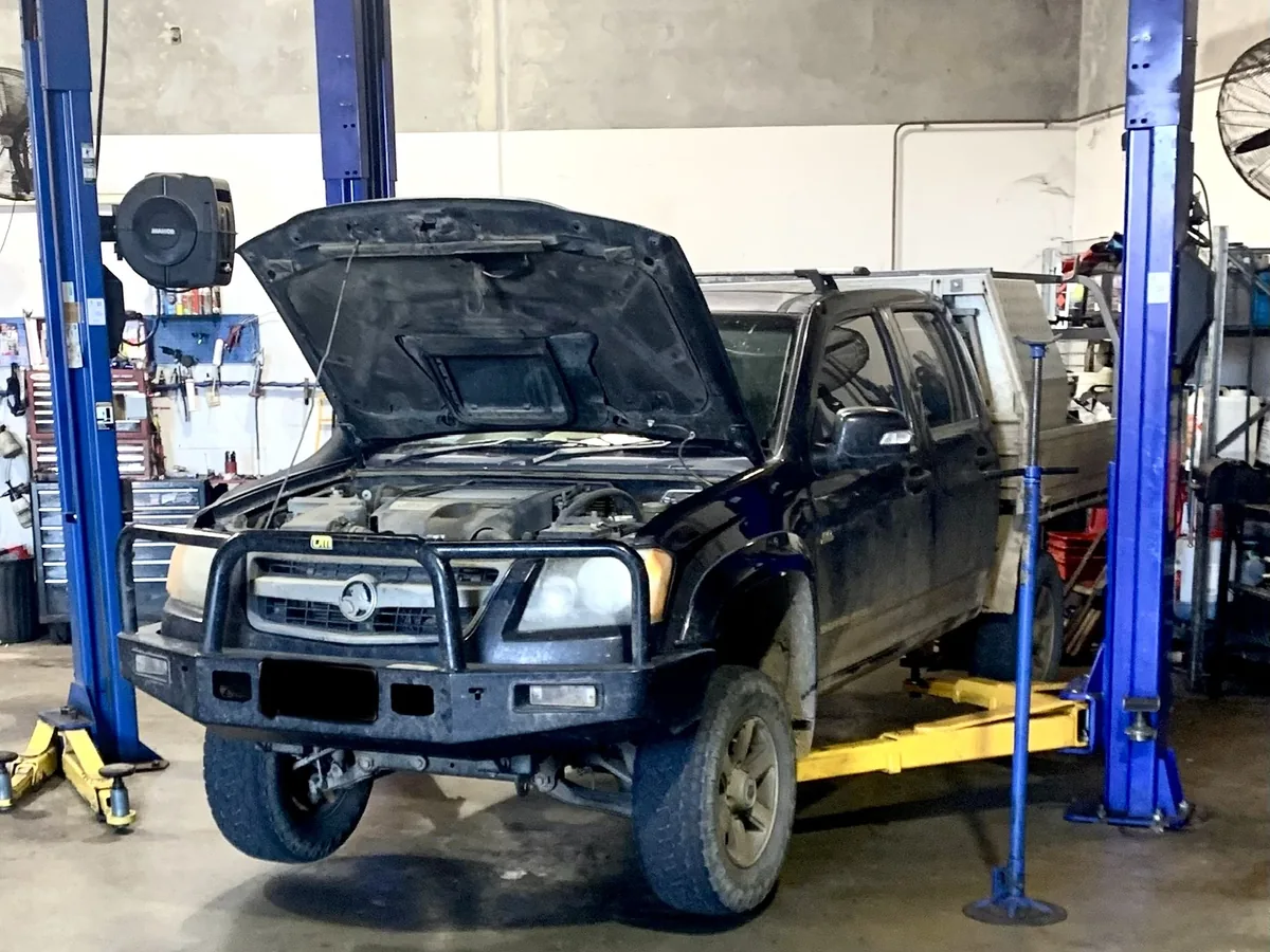 A black ute with its bonnet open on a two-post hoist.