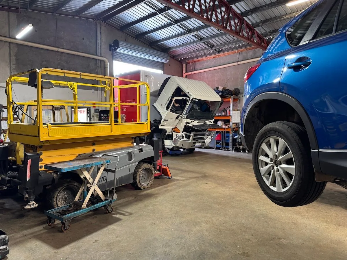 A blue car on a hoist beside a yellow scissor lift inside the workshop.