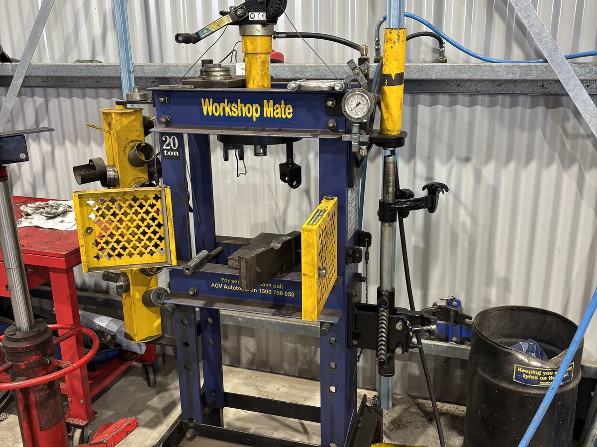 A blue hydraulic workshop press with yellow guards beside it.