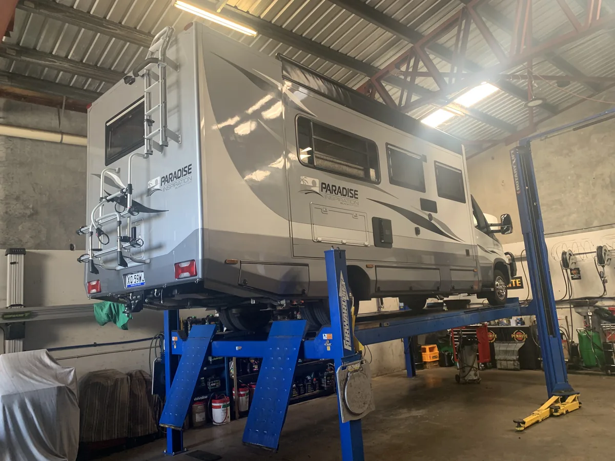 A caravan raised on a blue hoist in the workshop.