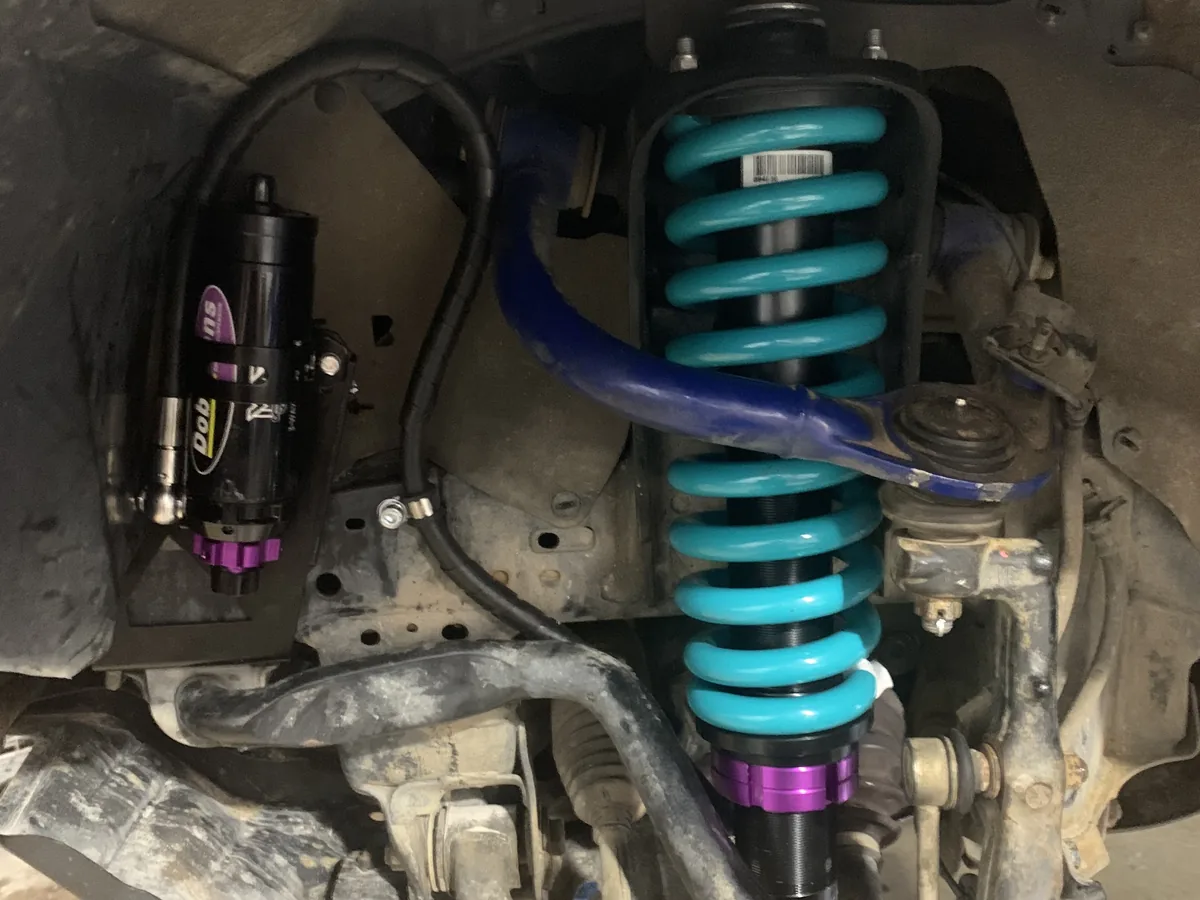 A coil-over shock absorber with a teal spring fitted inside a front wheel arch.