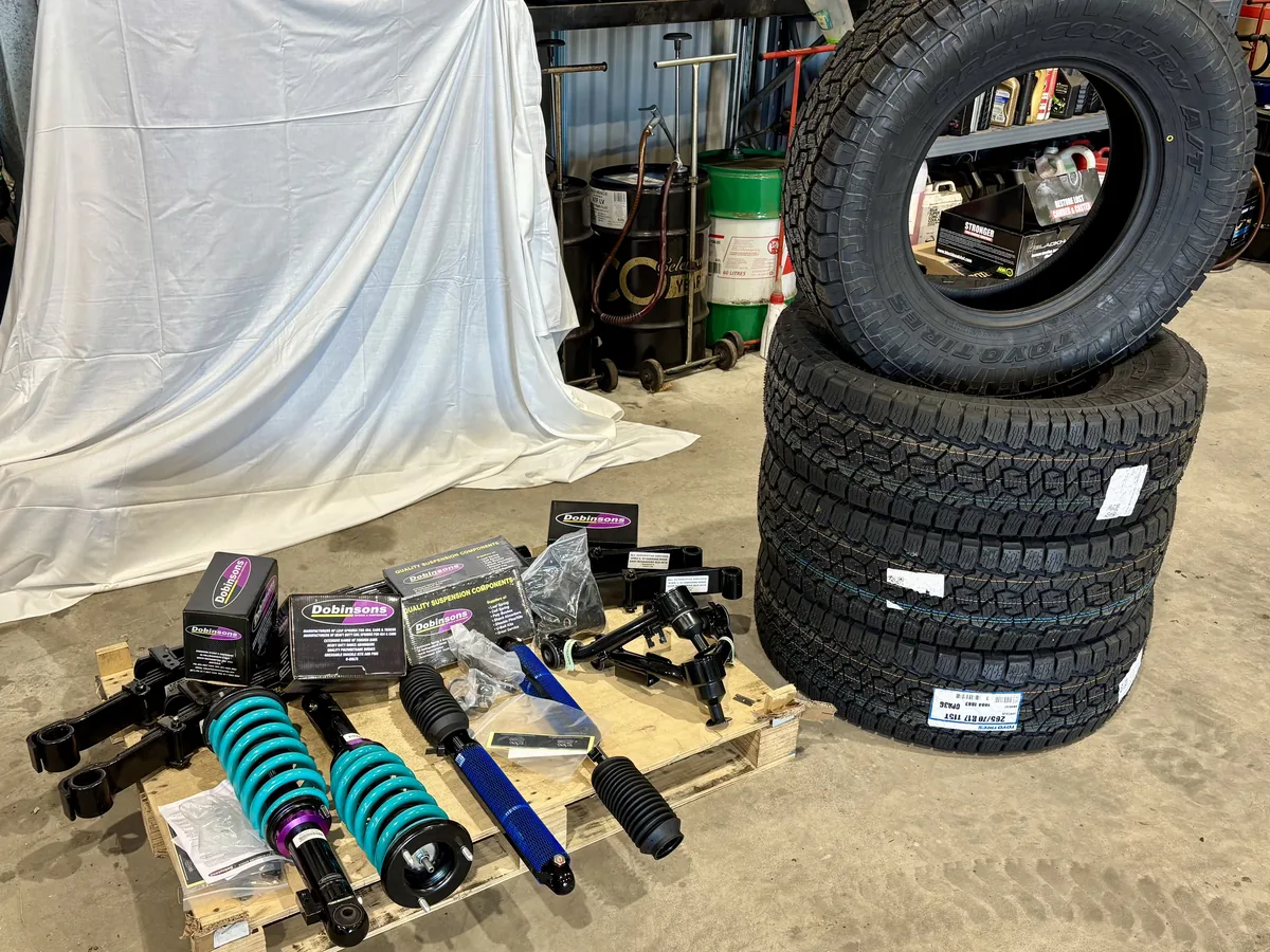 A Dobinsons suspension kit on a pallet beside a stack of four tyres.