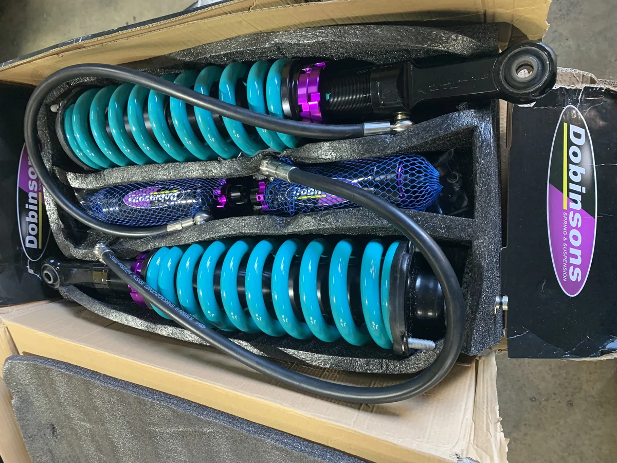 Two teal coil-over springs with shock absorbers laid in their box.