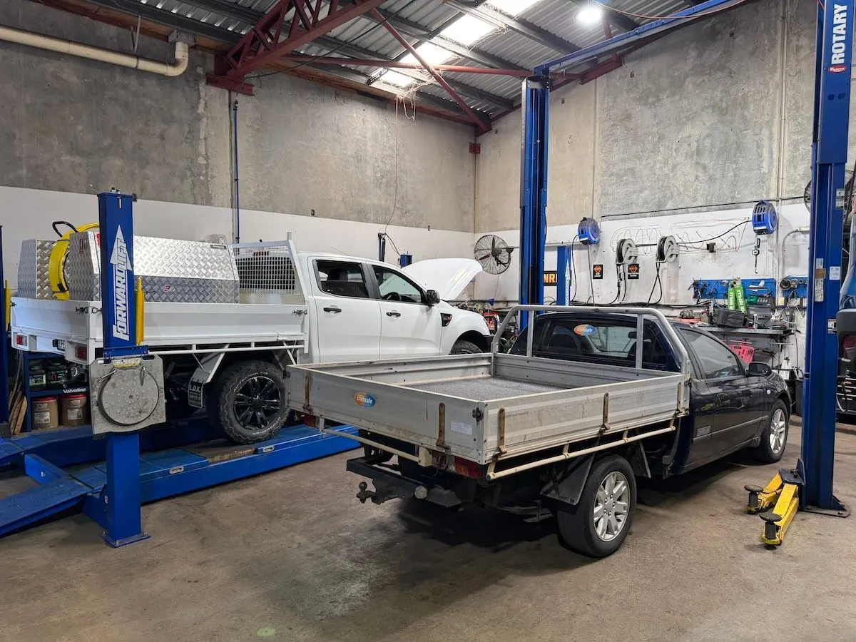 Two utes raised on blue hoists in the workshop, one with its bonnet open.