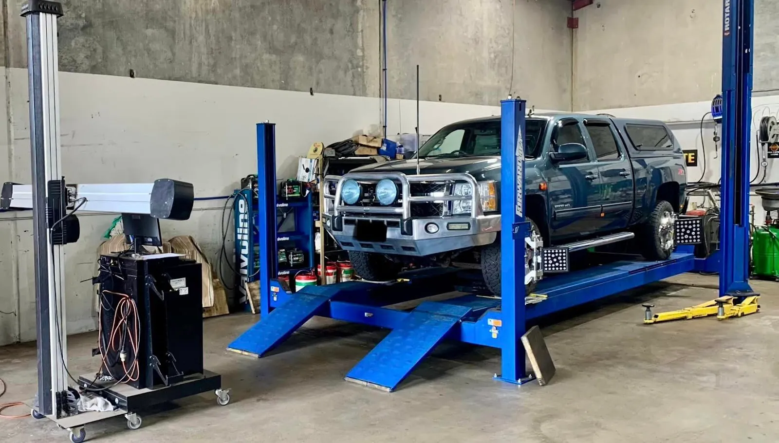 A ute on a blue wheel alignment rack with measuring heads fitted to its wheels.