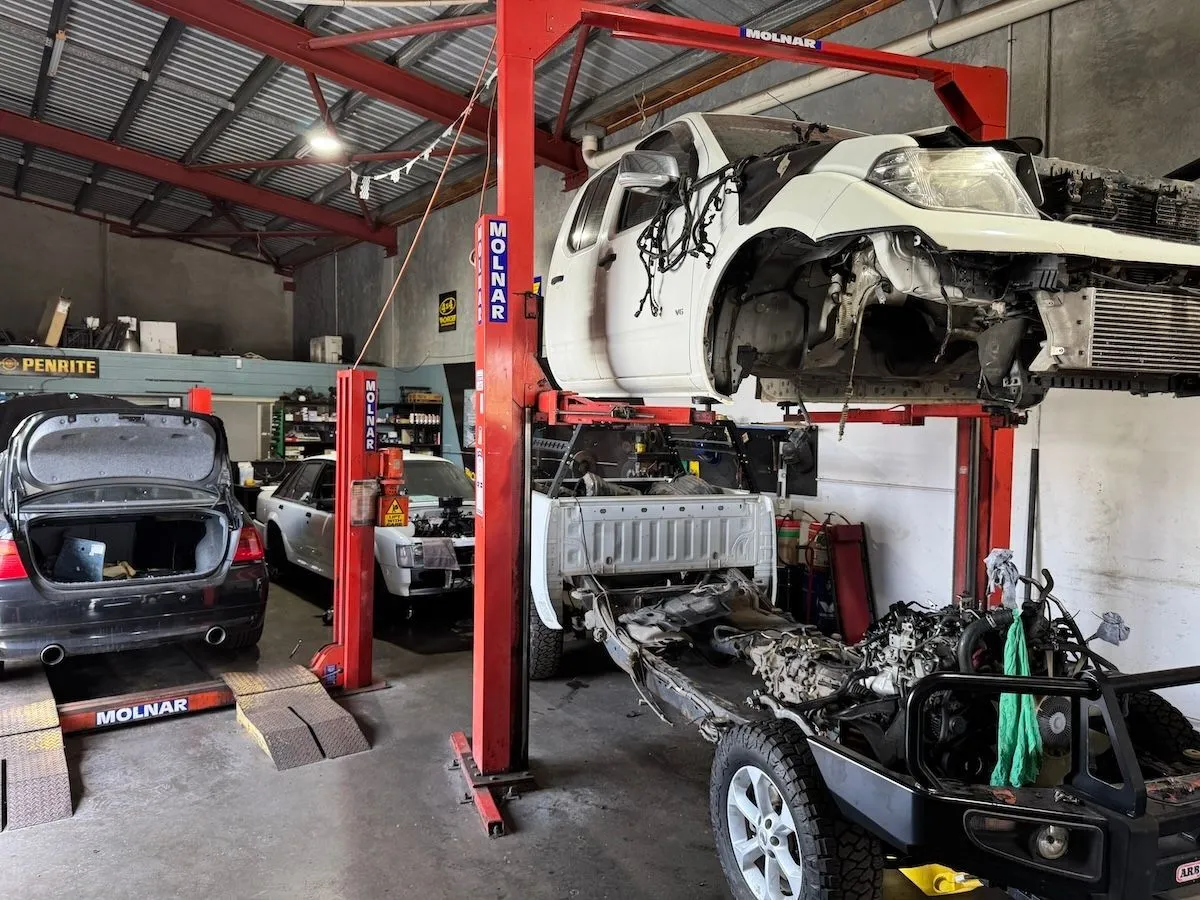 A vehicle raised on a red two-post hoist with its front end stripped down.