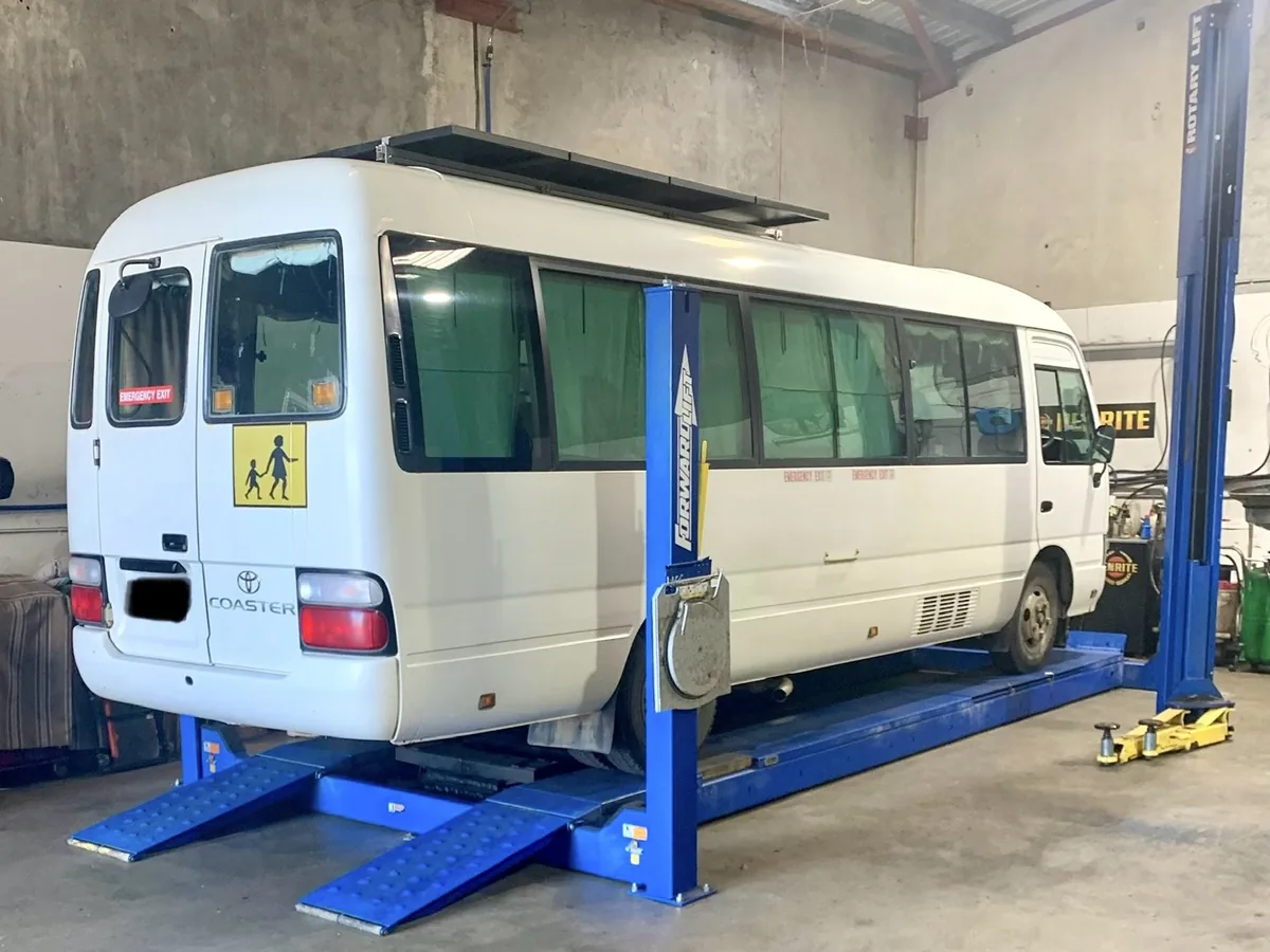 A white minibus raised on a blue four-post hoist in the workshop.