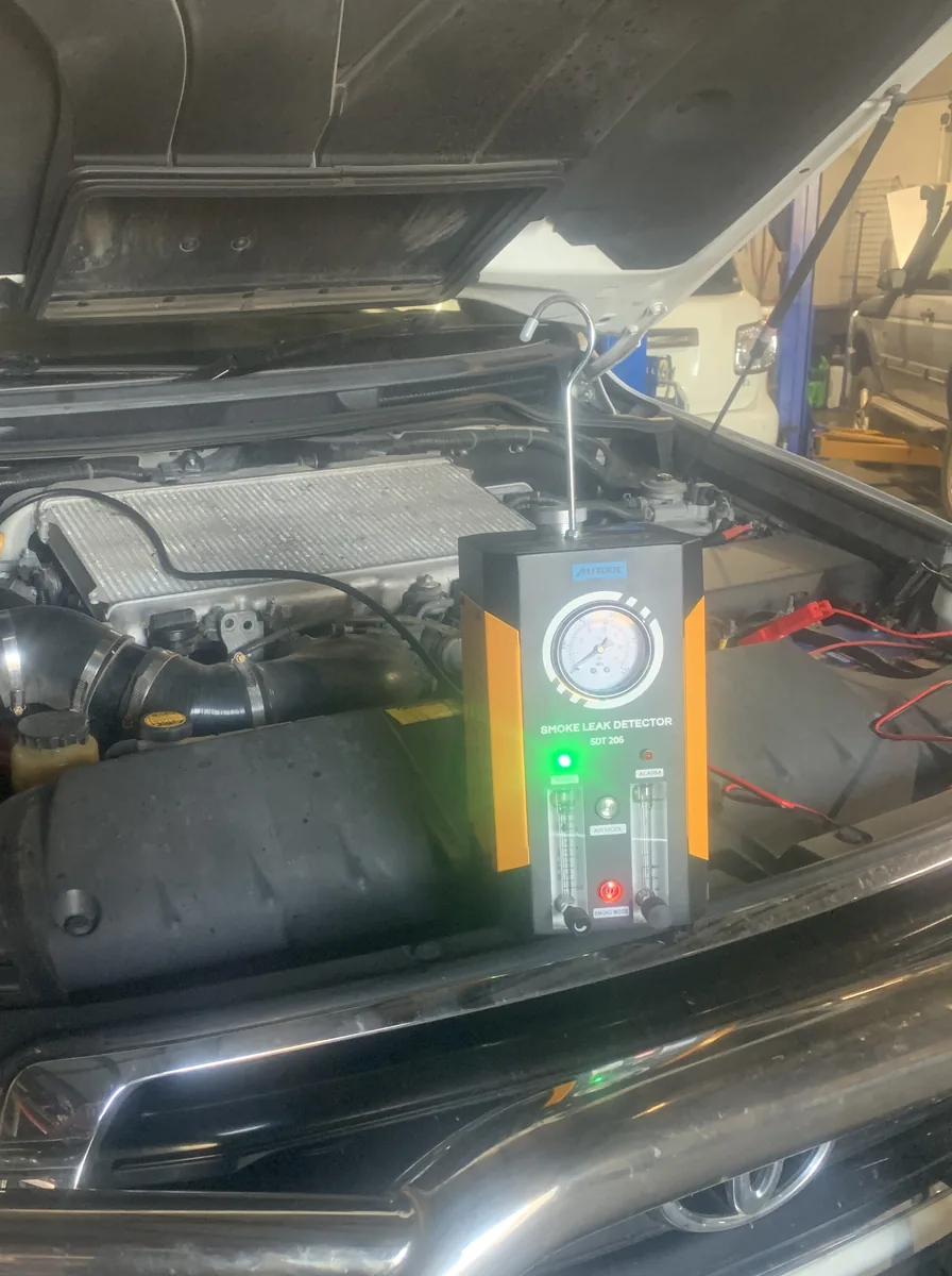 A smoke leak detector with its pressure gauge and green power light standing in front of an open engine bay.