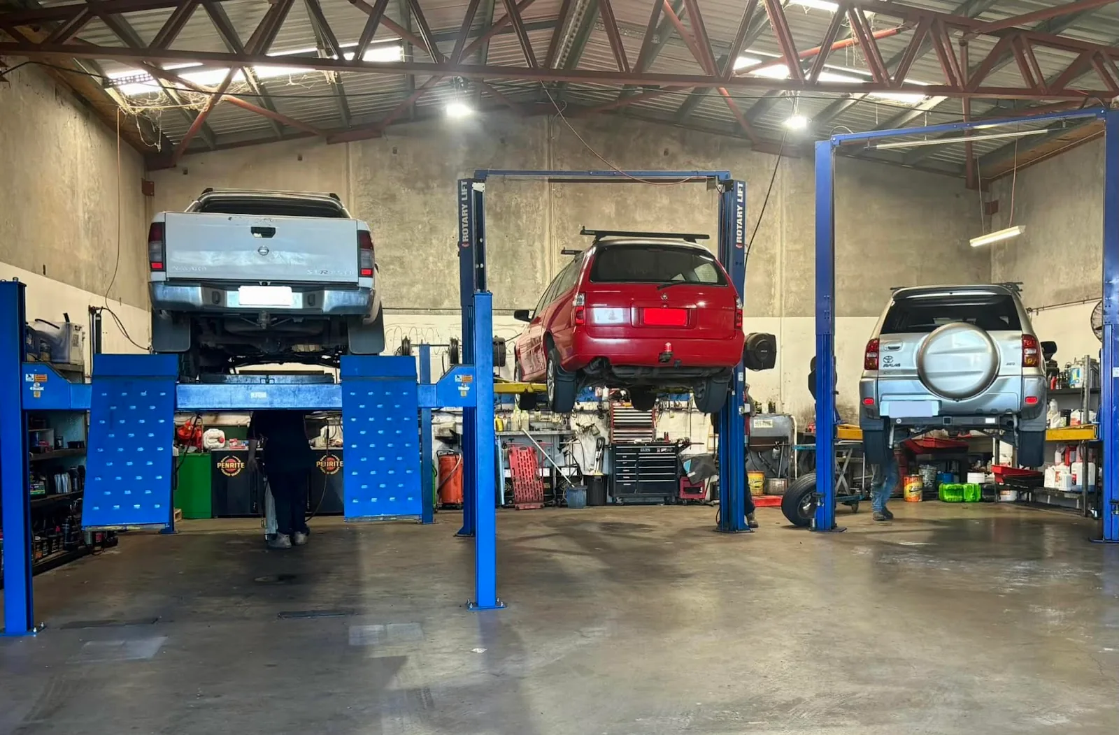 Three vehicles raised on blue two-post hoists in the workshop.